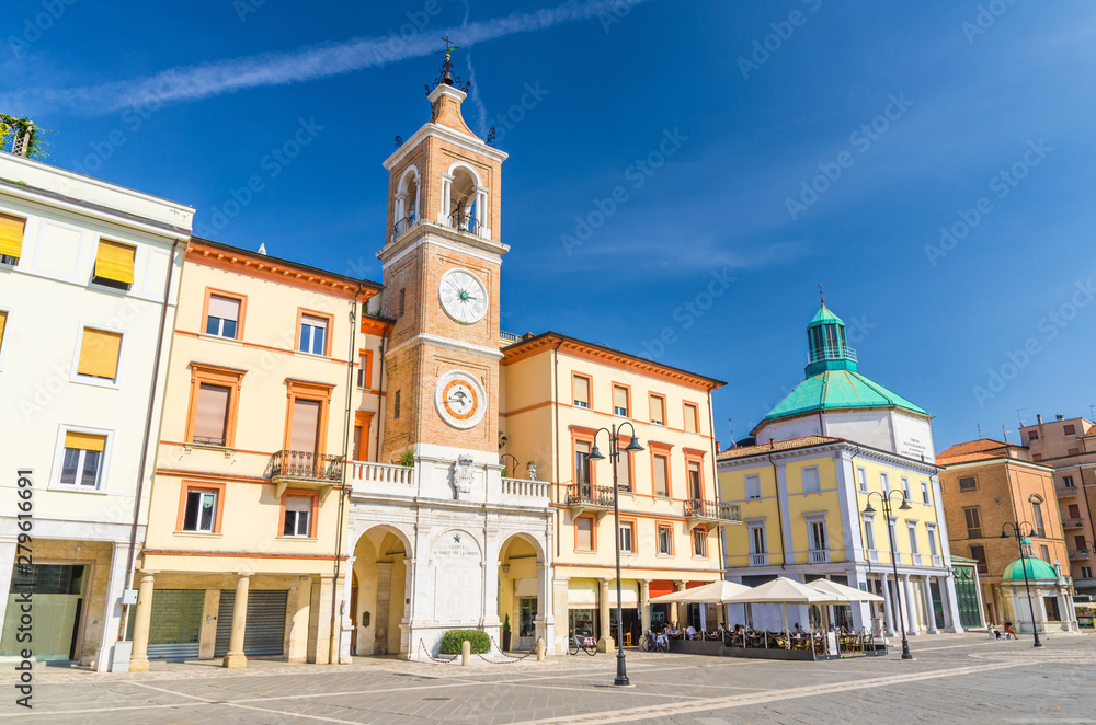 Piazza Tre Martiri Three Martyrs square with traditional buildings with clock and bell tower in old historical touristic city centre Rimini with blue sky background, Emilia-Romagna, Italy