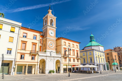 Piazza Tre Martiri Three Martyrs square with traditional buildings with clock and bell tower in old historical touristic city centre Rimini with blue sky background, Emilia-Romagna, Italy photo