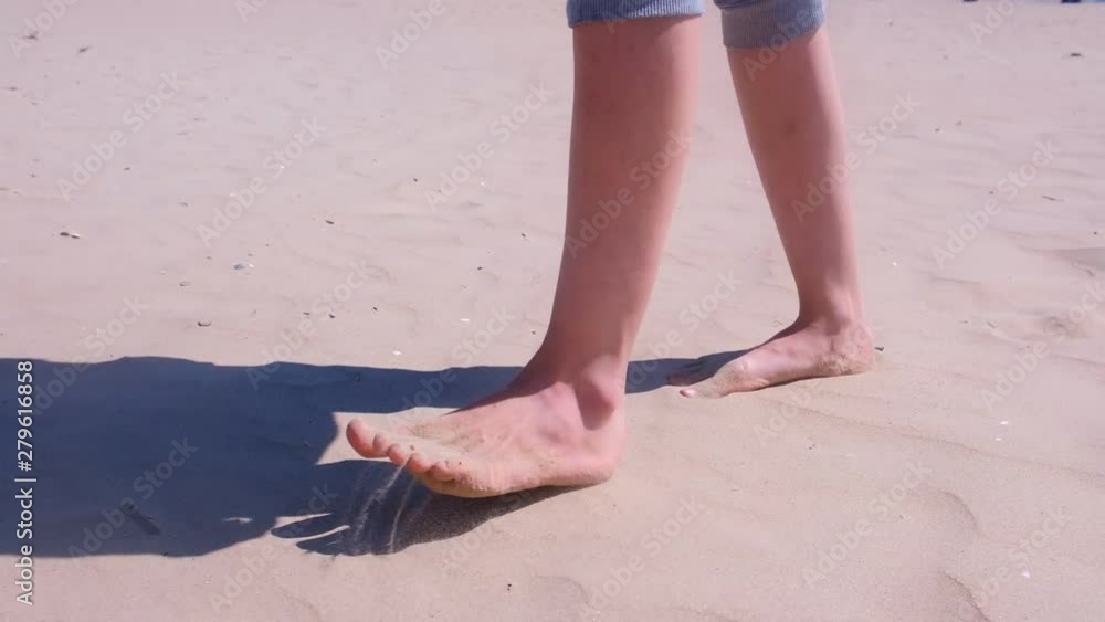 Barefooted girl traveller go by seashore on hot sand. Woman tourist walks on sand at sea beach resting on vacation, legs closeup. Tourism and travel concept. Barefooted girl traveller go by seashore on hot sand. Woman tourist walks on sand at sea beach resting on vacation, legs closeup. Tourism and travel concept.