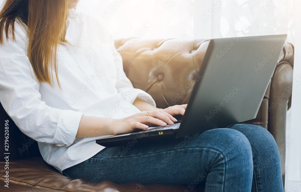 Naklejka premium Young asian woman sitting on sofa and using laptop working in cafe