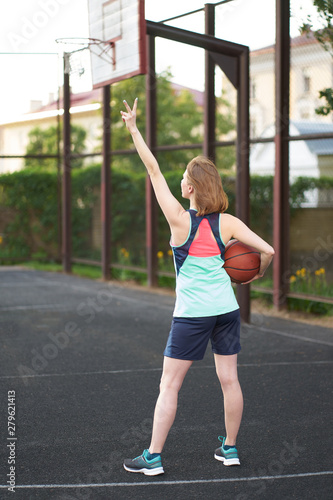 Redhead smiling caucasian girl shows victory sign with her fingers at outdoor street basketball court © Kiryl Lis