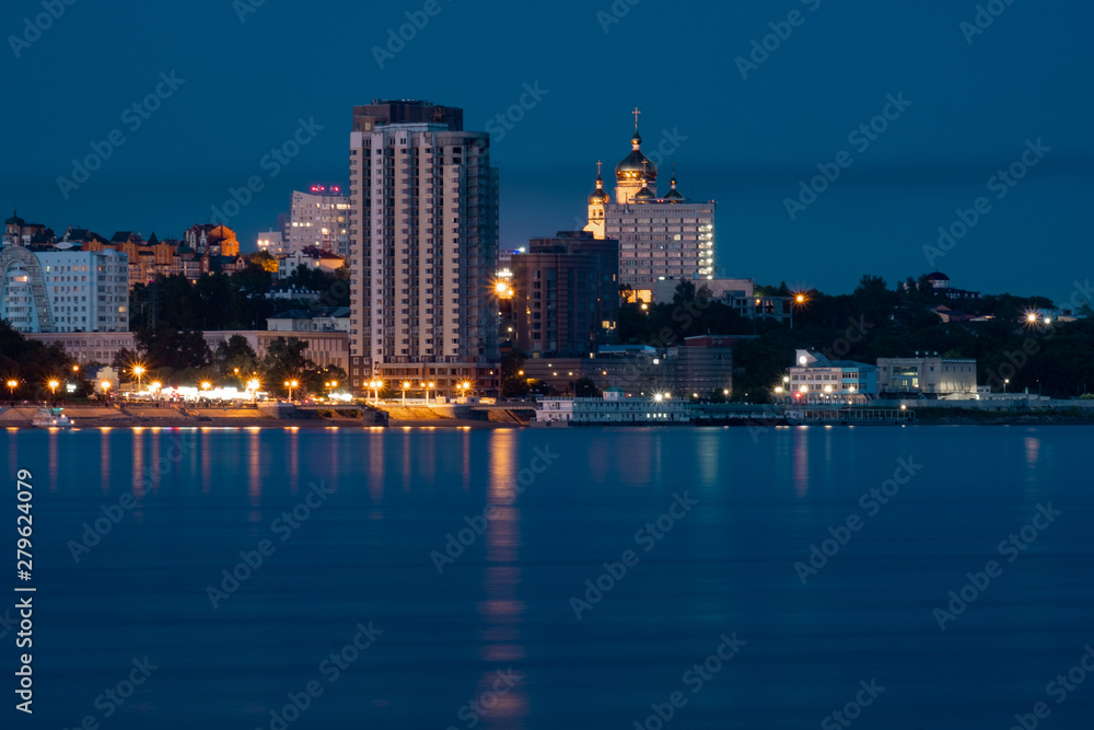 Night View of the city of Khabarovsk from the Amur river. Blue night sky. The night city is brightly lit with lanterns.