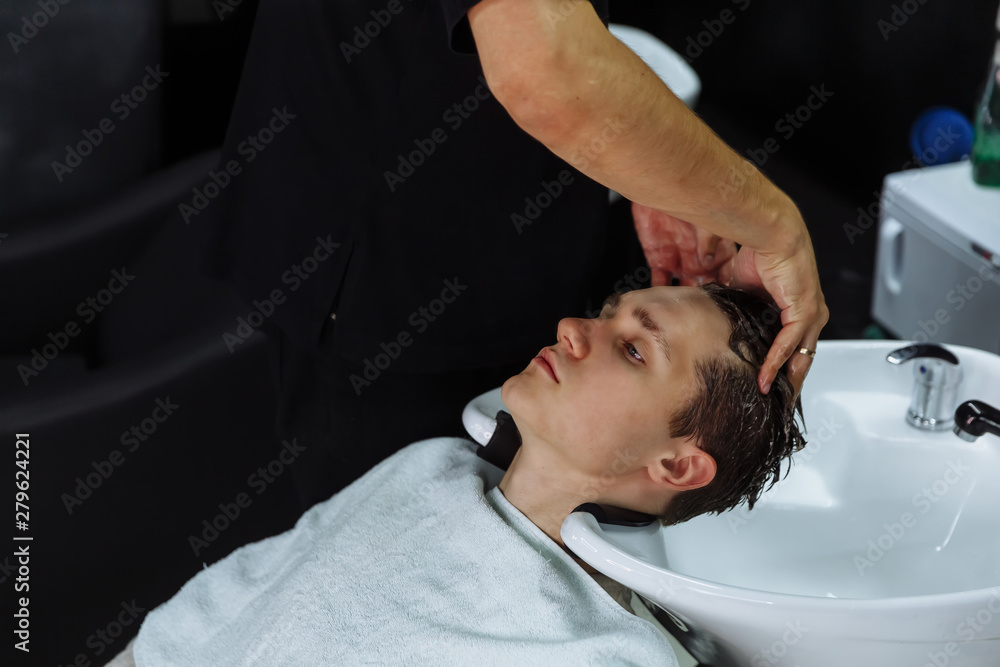Attractive male is getting a modern haircut in barber shop. Profile view of a young man getting his hair washed and his head massaged in a hair salon Attractive male is getting a modern haircut in barber shop. Profile view of a young man getting his hair washed and his head massaged in a hair salon