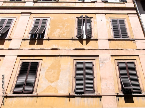 Photography The image of an old yellow authentic apartment and its wooden window in sunny day, Italy