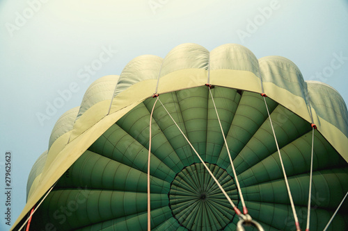 Hot air balloon flying in the blue sky in Green colour fabric parachute open and the ropes hook with the basket