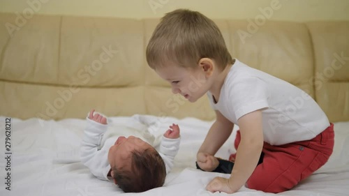 Funny little boy caress and kiss newborn baby,happy blond hair toddler