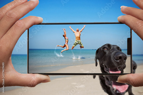 Woman photographing on cell phone happy couple on the beach and dog.