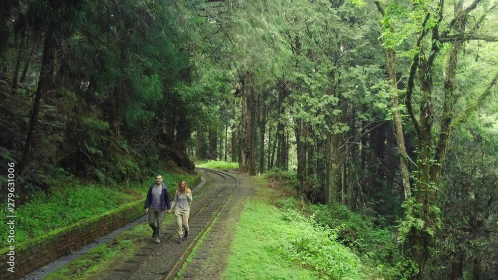 Young Couple of Tourists Walking along Old Abandoned Railroad in Alishan Scenic Area Forest in Taiwan. Aerial View Young Couple of Tourists Walking along Old Abandoned Railroad in Alishan Scenic Area Forest in Taiwan. Aerial View