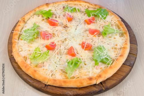 Pizza with chicken and cheese, tomatoes and lettuce on top on wooden board. Side view
