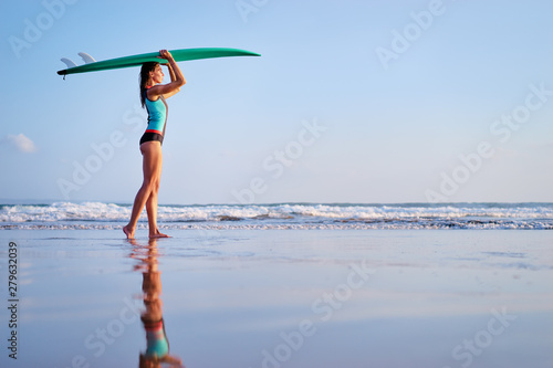 It's time for surfing! Hobby and vacation. Pretty young woman holding surf board on the sea shore.