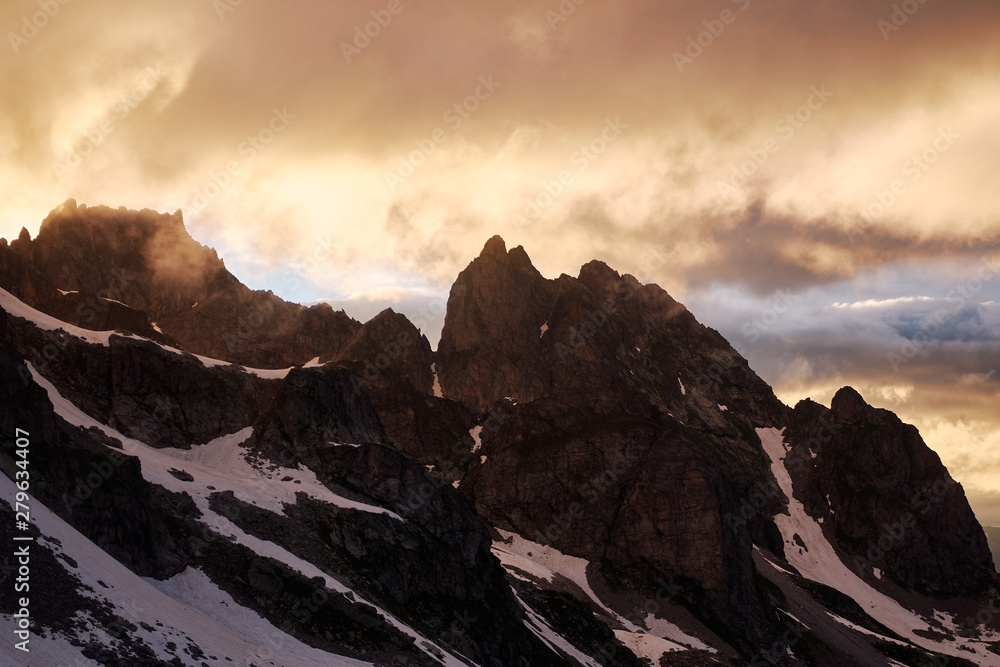 Obraz premium Stunning Sunset in the mountains cloudscape. Silhouette of snowy rock under the dramatic cloudy sky. Sozarukova Top, Caucasian Mountains in Karachay-Cherkessia, Russia.