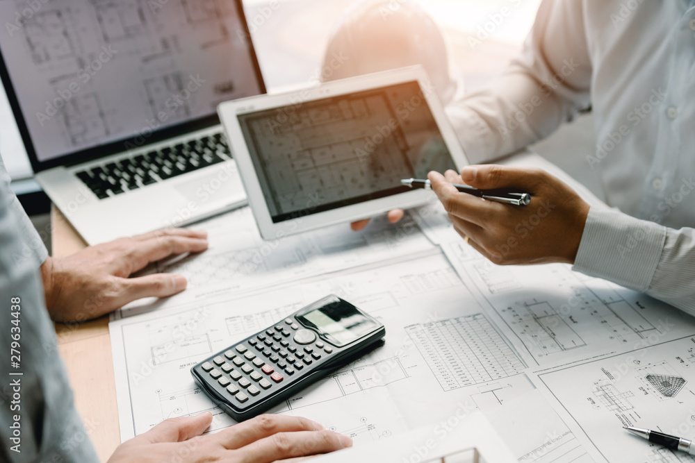Two engineering working together and using digital tablet looking blueprint and analysis with architectural plan on desk. Two engineering working together and using digital tablet looking blueprint and analysis with architectural plan on desk.