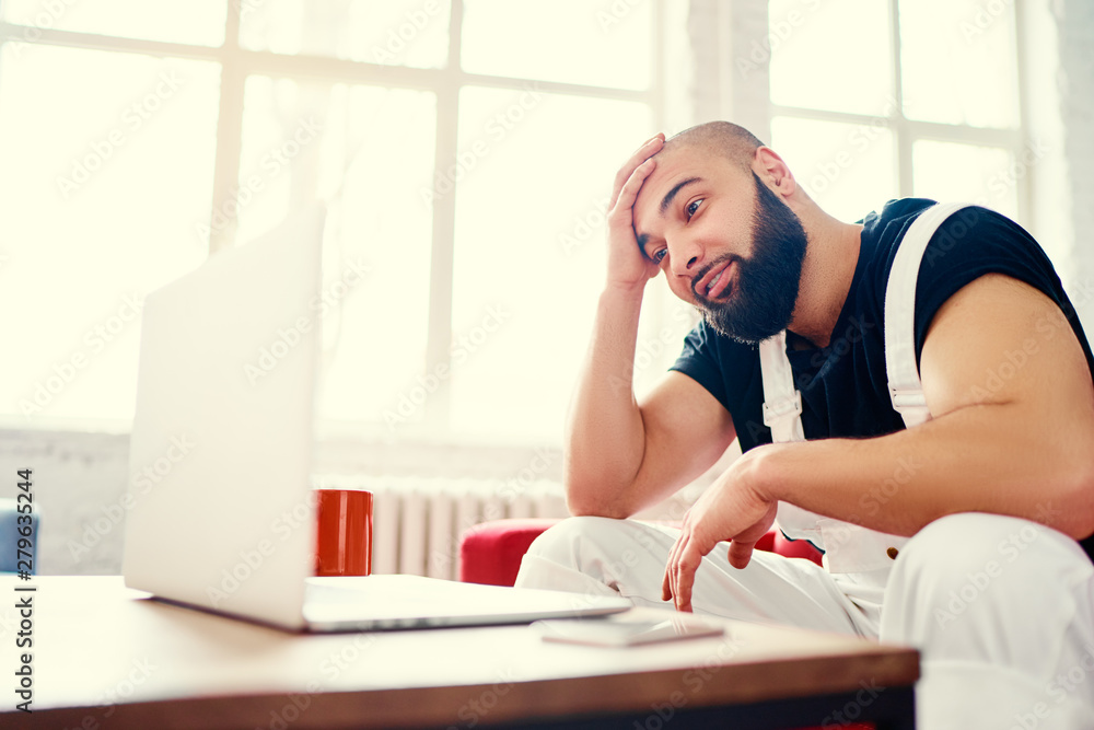 Stressed and tired young man with beard working on laptop computer at home. Stressed and tired young man with beard working on laptop computer at home.