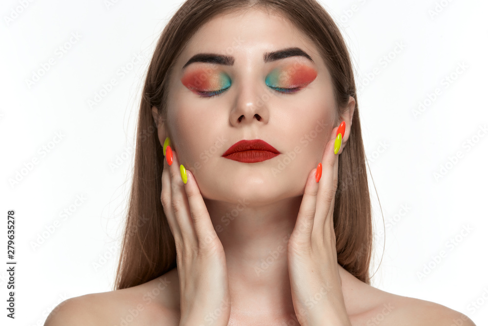 Closeup portrait of beautiful young woman with bright color make-up holding hands with bright manicure close to face Closeup portrait of beautiful young woman with bright color make-up holding hands with bright manicure close to face