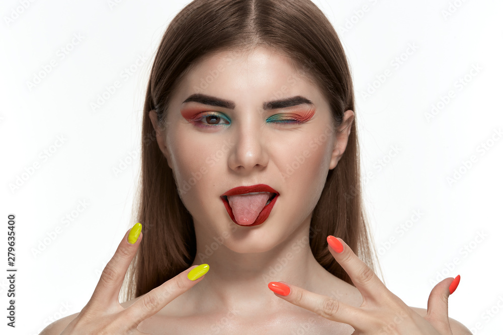 Closeup portrait of beautiful young woman with bright color make-up holding hands with bright manicure close to face sliping a wink and showing tongue. Closeup portrait of beautiful young woman with bright color make-up holding hands with bright manicure close to face sliping a wink and showing tongue.