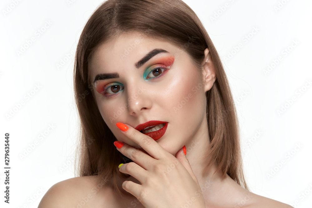 Closeup portrait of beautiful young woman with bright color make-up holding hands with bright manicure close to face Closeup portrait of beautiful young woman with bright color make-up holding hands with bright manicure close to face
