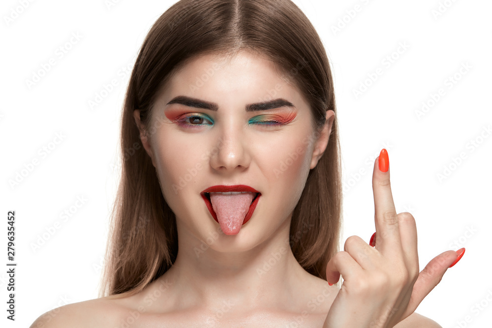 Closeup portrait of beautiful young woman with bright color make-up holding hands with bright manicure close to face sliping a wink, showing tongue and a finger with a middle finger sign. Closeup portrait of beautiful young woman with bright color make-up holding hands with bright manicure close to face sliping a wink, showing tongue and a finger with a middle finger sign.