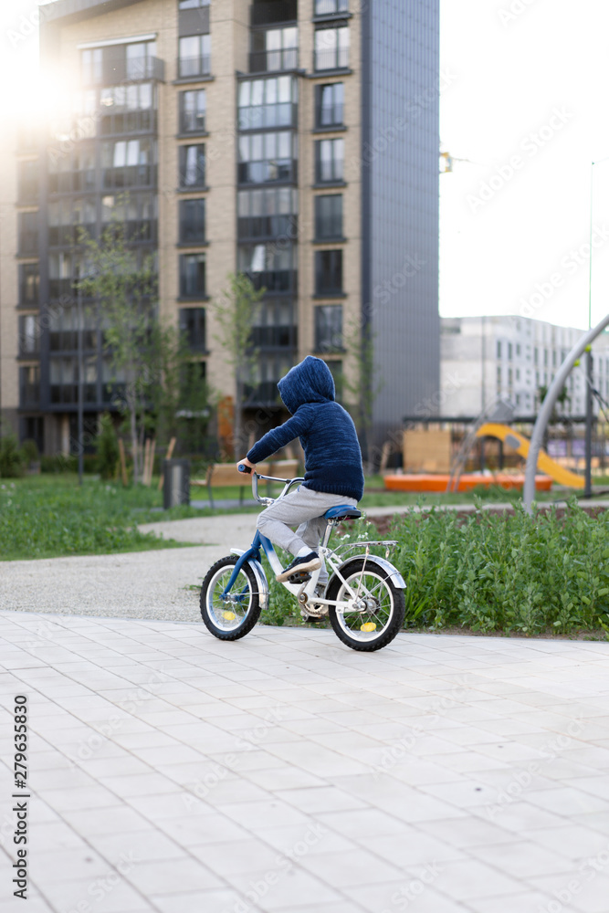 safety in a modern European city. A little happy boy rides a bicycle through a closed courtyard in a multi-storey urban building. safety in a modern European city. A little happy boy rides a bicycle through a closed courtyard in a multi-storey urban building.