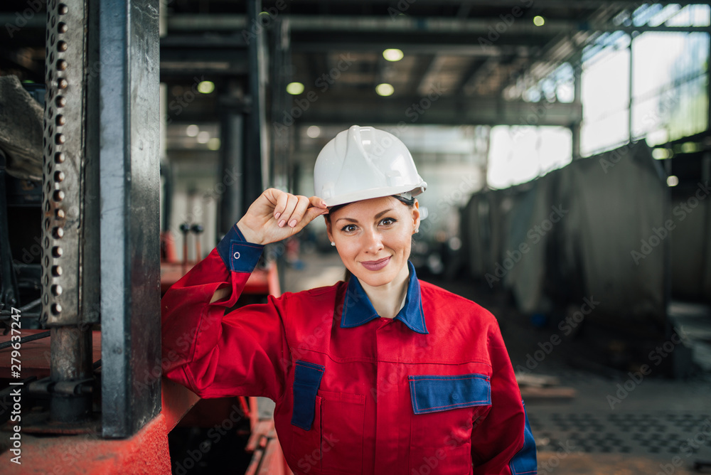 Portrait of a beautiful female factory worker wearing uniform and hardhat at factory hall. Portrait of a beautiful female factory worker wearing uniform and hardhat at factory hall.