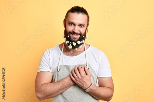 emotional sweet man with a beard decorated with flowers showing his affection. garderner fell in lovee. close up portrait. isolated yellow background I love you photo