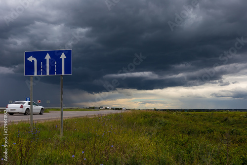 Road sign of the direction of movement against the sky with dark rain clouds. Choosing a path.