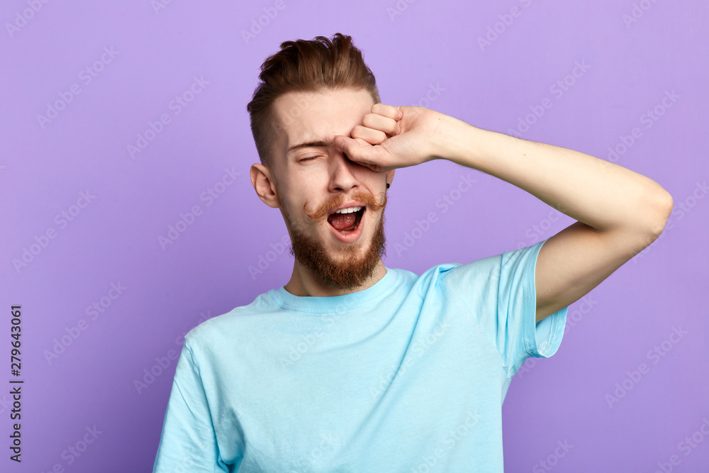 Handsome bored sleepy bearded man touching his eyes after long overwork on new project, wants to sleep in the morning, close up portrait. isolated blue background, studio shot Handsome bored sleepy bearded man touching his eyes after long overwork on new project, wants to sleep in the morning, close up portrait. isolated blue background, studio shot
