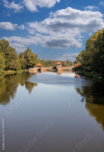 View from the river "Weisse Elster" in Leipzig with trees, bridges and a weir at blue sky