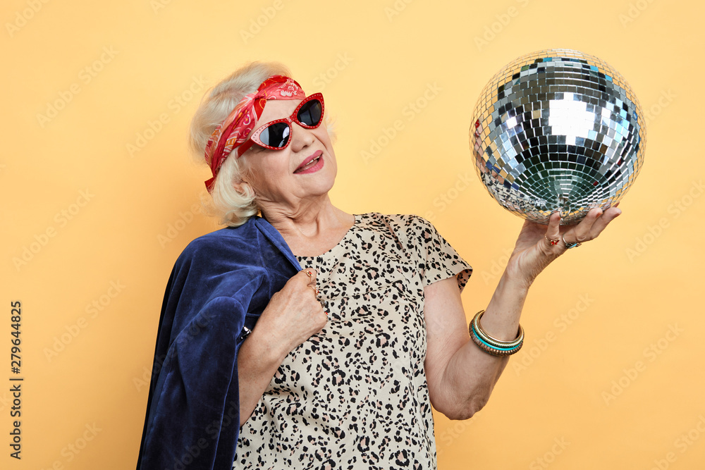 Fototapeta premium smiling pretty old woman looking at the ball, old lady remember her youth. isolated yellow background. studio shot