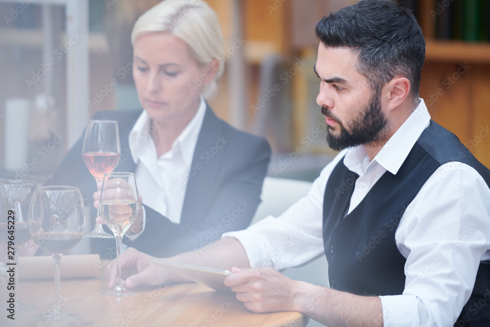 Young man with tablet and glass of white wine examining its characteristics