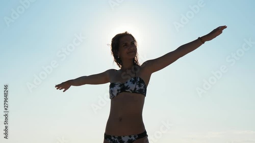 thrilling portrait of young awesom wet lady in swimsuit with rosed hands on the beach on the clear sky background, Slow motion photo