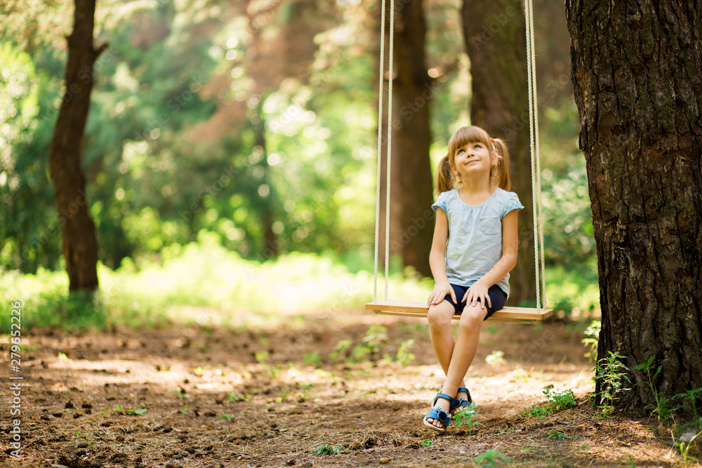 Happy Little girl on a swing in the summer park