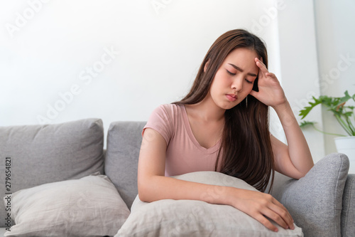 Asian young woman holding her head,she has a headache sitting on sofa couch in living room at home.