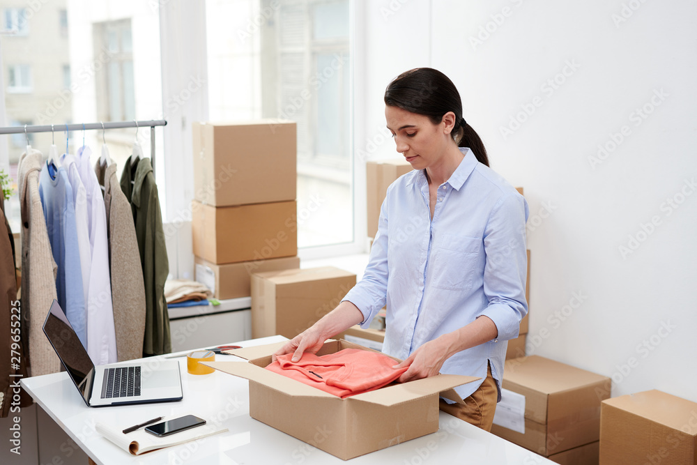 Young attractive woman in casualwear putting folded red pullover into box Young attractive woman in casualwear putting folded red pullover into box