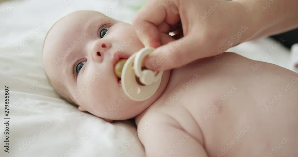 Restless newborn baby wriggling in a cot as the mother inserts a dummy which the child spits out trying to put a thumb in its mouth Restless newborn baby wriggling in a cot as the mother inserts a dummy which the child spits out trying to put a thumb in its mouth