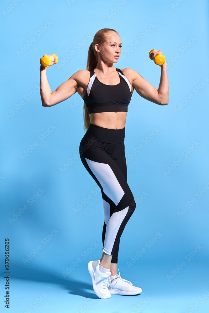 fitness, cross fit , dieting concept - young sporty woman with light dumbbells working out in the health studio. isolated blue background. studio shot. wellness, wellbeing fitness, cross fit , dieting concept - young sporty woman with light dumbbells working out in the health studio. isolated blue background. studio shot. wellness, wellbeing