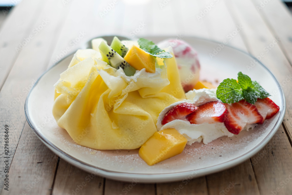 Crepe and ice cream with fresh fruit on wooden table.