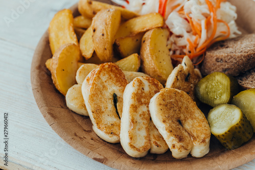 Tasty grilled fish with fried potatoes, cucumber, cabbage and woods in a paper plate on a wooden table. takeaway street food