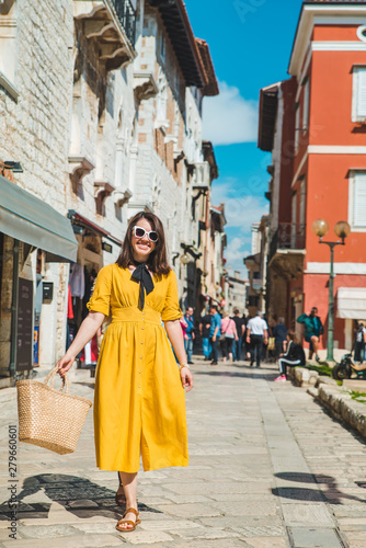 tourist woman in yellow sundress walking by small croatian city street