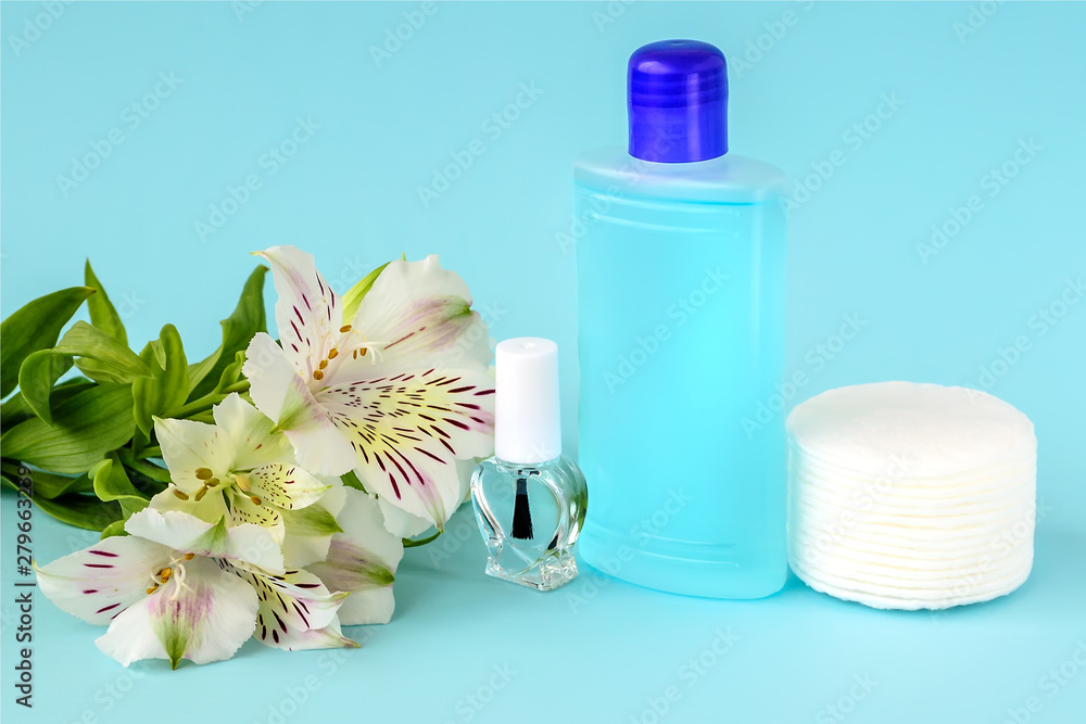 Glass bottle with colorless nail polish, plastic bottle with nail varnish remover, cotton pads and white flowers on a blue background. Manicure, pedicure, nail care products. Glass bottle with colorless nail polish, plastic bottle with nail varnish remover, cotton pads and white flowers on a blue background. Manicure, pedicure, nail care products.