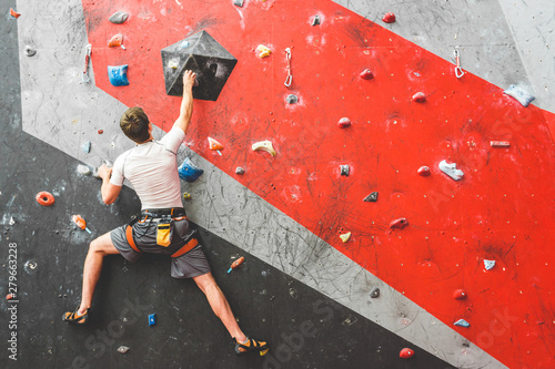 Sportsman climber moving up on steep rock, climbing on artificial wall indoors. Extreme sports and bouldering concept photo