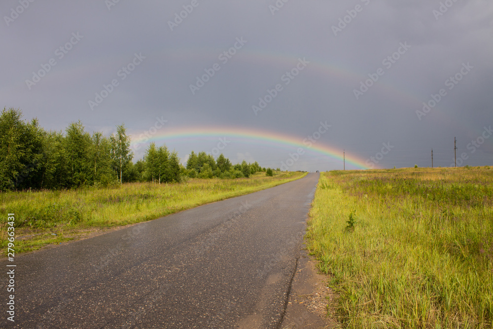 The road going to the horizon and a big rainbow in the sky