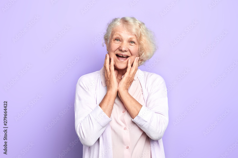 Old blonde girl touching face with palms, expresses happiness and joy. isolated blue background. studio shot woman has heard that she would get big pension Old blonde girl touching face with palms, expresses happiness and joy. isolated blue background. studio shot woman has heard that she would get big pension