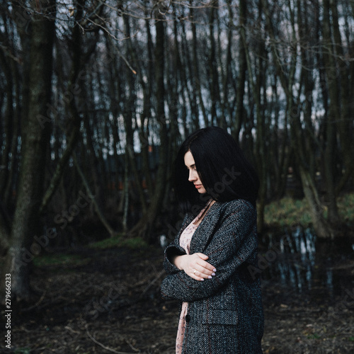 young girl in a dark gray coat standing by the lake