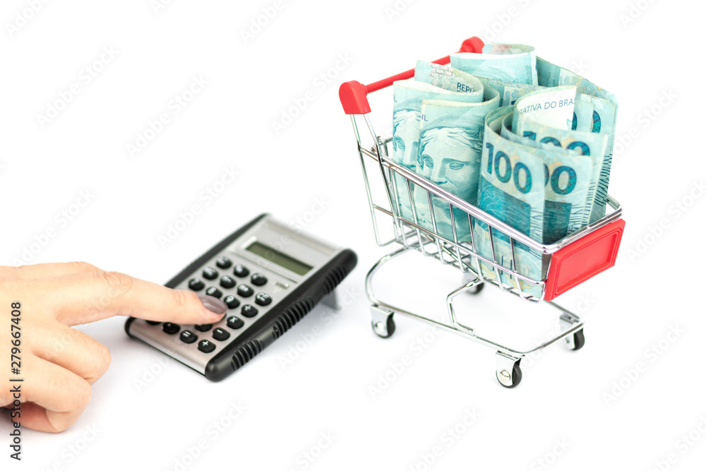 Female hand puching brazilian notes one hundred (100) reais, shopping cart or supermarket trolley and calculator and calculator, business finance shopping concept. Brazil money. Female hand puching brazilian notes one hundred (100) reais, shopping cart or supermarket trolley and calculator and calculator, business finance shopping concept. Brazil money.