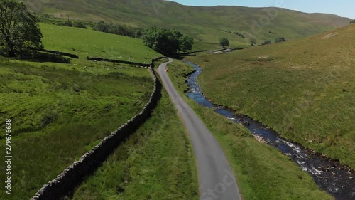 An ascending aerial shot of Barbon Beck, Carnforth, Lancashire, England. This stunning countryside features a stream running alongside a small country lane. photo