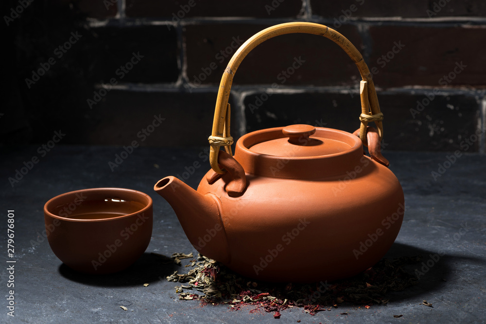 brown ceramic teapot and cup of tea on a dark background