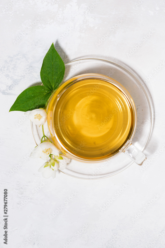 glass cup with green tea on a white background and a branch of jasmine, vertical top view glass cup with green tea on a white background and a branch of jasmine, vertical top view
