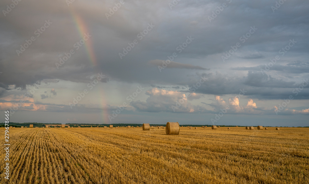 beautiful multicolored rainbow over a sloping wheat field with large rolls of straw