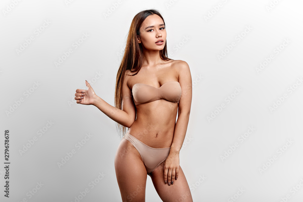 Obraz premium seductive tanned woman in beige bra showing thumb up. close up photo. isolated white background. studio shot , best choice. fitness, sport, lifestyle, effective training program. good results in diet