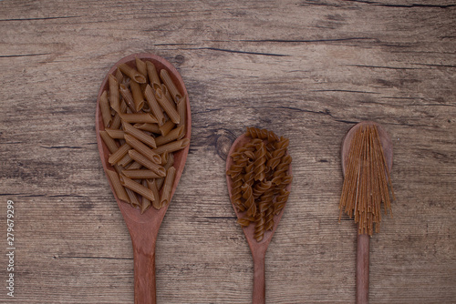 spoons with a variety of raw pasta in a wooden background